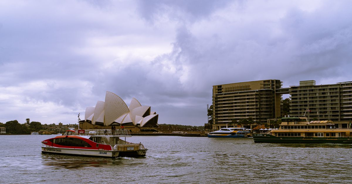 Scenic view of Sydney Opera House and bustling harbor in cloudy weather, New South Wales, Australia.